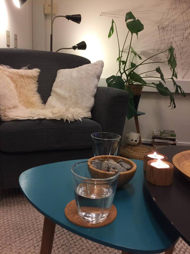 Klinikken: en grå sofa med skindpuder, et lille blåt bord med vandglas, fyrfadslys og en plante